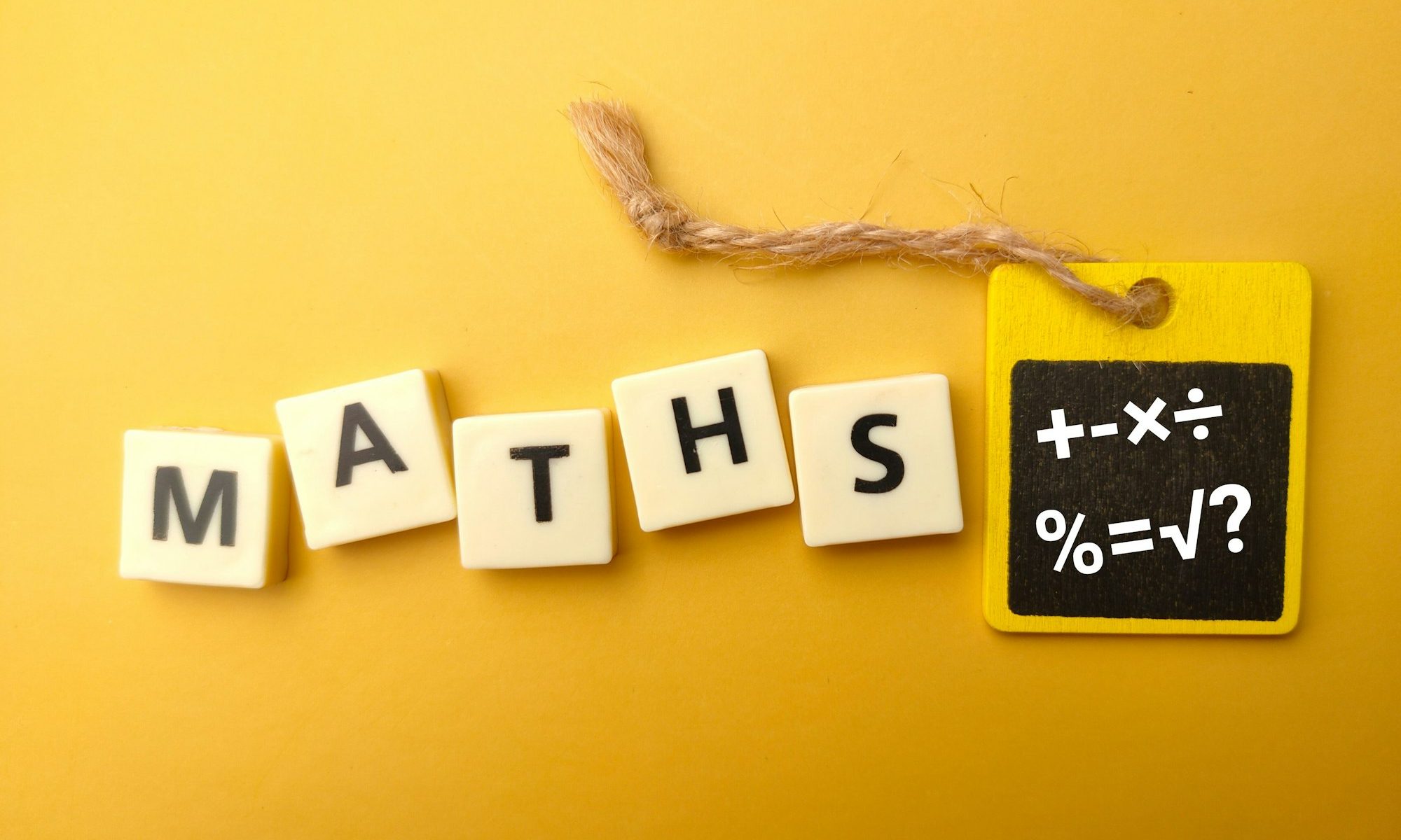 Cubes with the word MATHS and math symbols on blackboard on yellow background-education concept